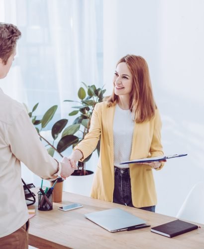 happy-recruiter-holding-clipboard-and-shaking-hands-with-employee-in-modern-office.jpg